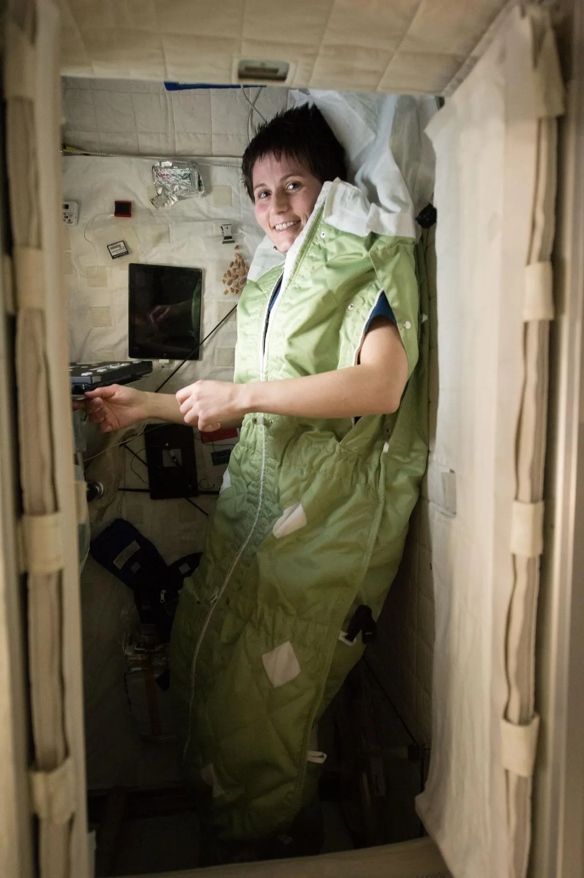 A astronauta Samantha Cristoforetti dentro de um saco de dormir verde preso à parede de sua cabine na estação