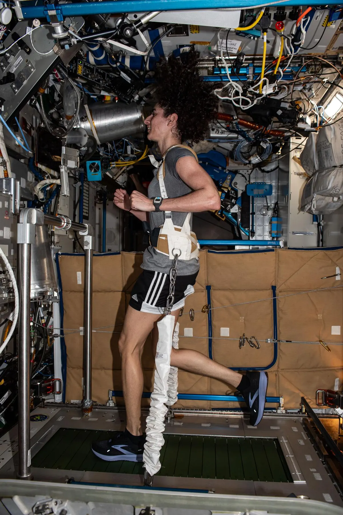 A astronauta Jasmin Moghbeli correndo na esteira T2, presa por um arnês com elásticos ligados ao piso da esteira