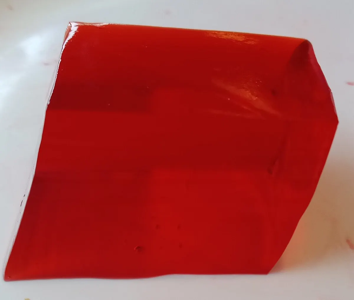 Pedaço de gelatina vermelha de morango com faces retas e brilhantes sobre um prato branco