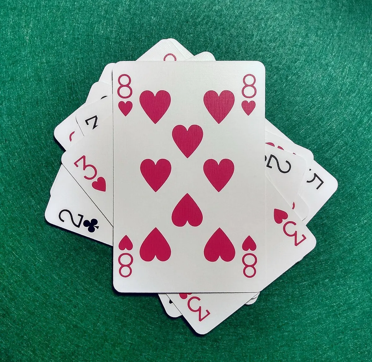 Um 8 de copas por cima de um monte de cartas de baralho espalhadas sobre um feltro verde